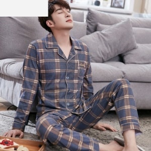 Trendy katoenen geruite pyjama voor mannen gedragen door een man zittend op een tapijt in een huis
