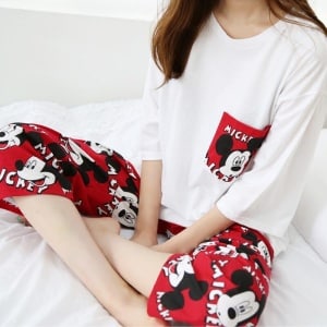 Rode en witte tweedelige pyjama met Mickey-motief gedragen door een vrouw zittend op een bed in de mode