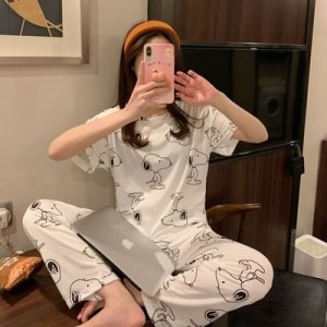Tweedelige pyjama met korte mouwen en hondenmotief gedragen door een zittende vrouw die een foto neemt in een huis