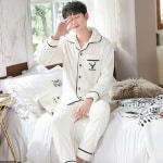 Herenpyjama van polyester met een lijnenspel gedragen door een man zittend op een bed in een huis
