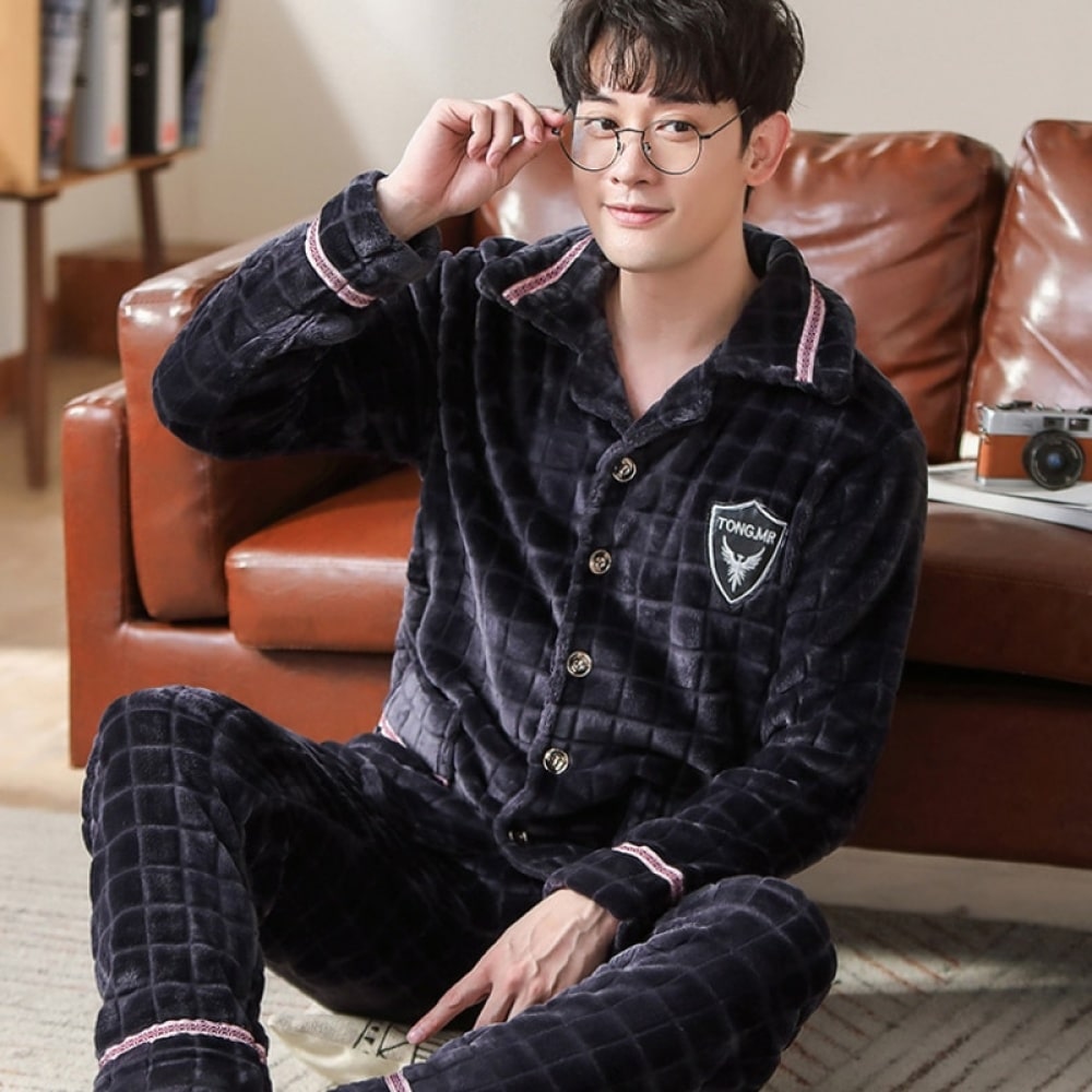 Flanellen herenpyjama met ruitjespatroon gedragen door een man zittend op een tapijt voor een bank in een huis