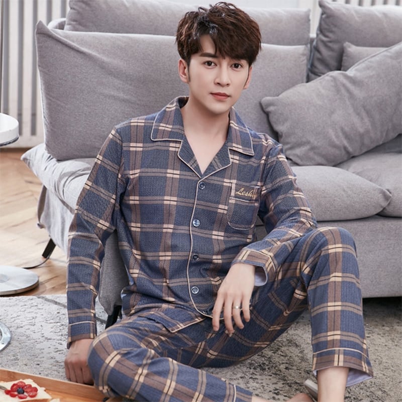 Dubbel geruite herenpyjama gedragen door een man zittend op een tapijt voor een bank in een huis