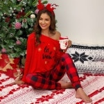 Pyjama met kerstprint voor vrouwen met blote schouders gedragen door een vrouw zittend op een tapijt voor een kerstboom in een huis