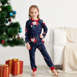 Pyjama met sneeuwvlokken en kerstmannenprint voor het gezin, gedragen door een klein meisje voor de kerstboom in een huis