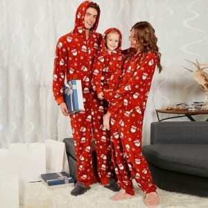 Kerstpyjamapak met capuchon voor het hele gezin, gedragen door een gezin voor een bank in een huis