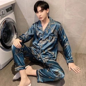 Herenpyjama in satijnblauw, gedragen door een man die voor een wasmachine in een huis zit