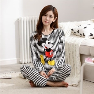 Gestreepte Mickey-pyjama voor vrouwen, gedragen door een vrouw zittend voor een bed in een huis