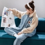 Lichtblauwe koppel fleece pyjama gedragen door een vrouw zittend op een bank in een huis
