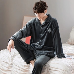 Effen fleece pyjama met kraag voor paar gedragen door een man zittend op een bed in een huis