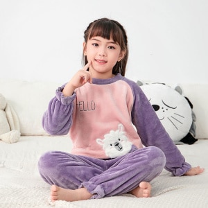 Paarse kinderpyjama van fleece gedragen door een klein meisje zittend op een bed in een huis