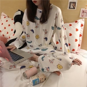 Witte herfstpyjama met cartoonpatroon voor vrouwen gedragen door een vrouw op een bed in een huis