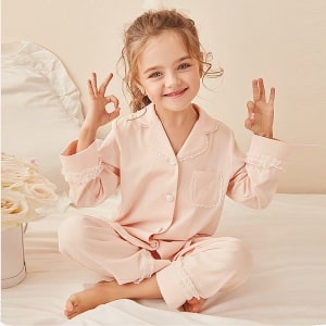Tweedelige pyjama in kant voor "doen zoals mama" met een klein meisje dat de pyjama draagt met een witte wieg en roze achtergrond