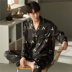 Zwarte katoenen pyjama met lange mouwen en omgeslagen kraag gedragen door een man zittend op een stoel in een huis