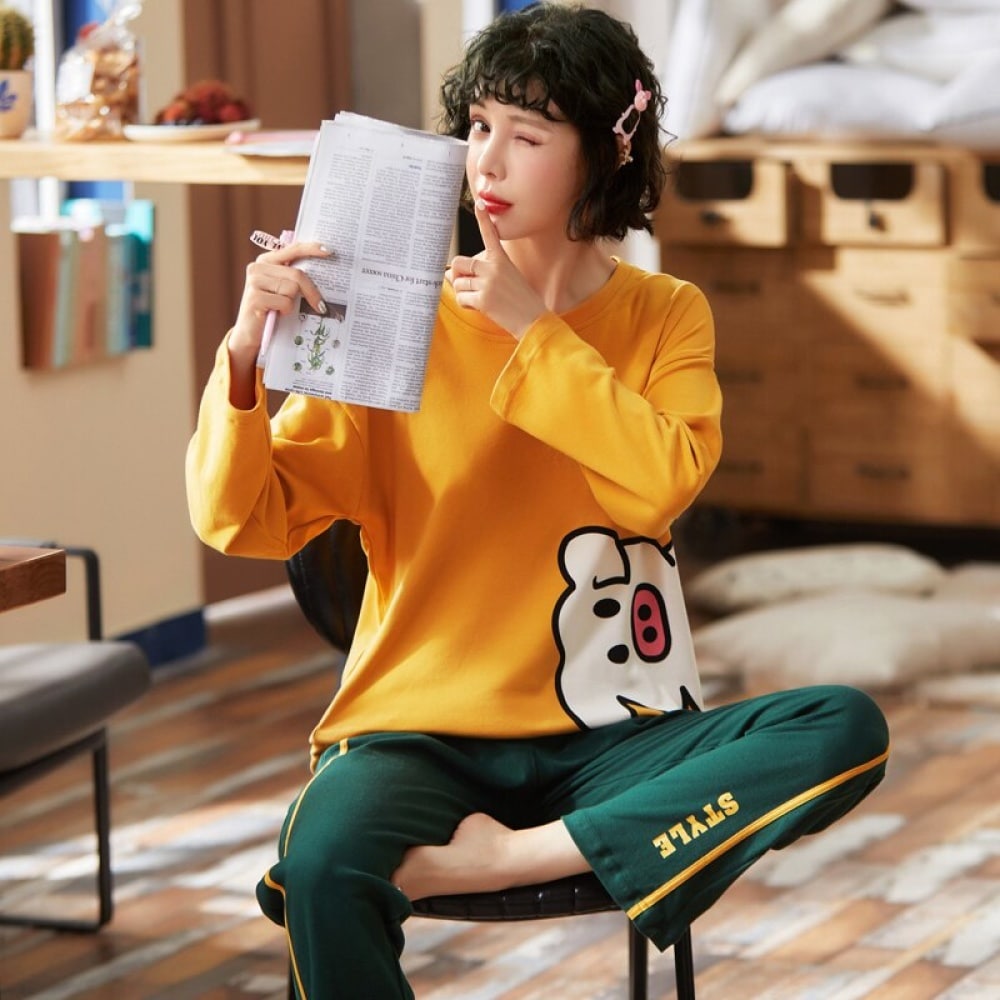 Katoenen pyjama met gele varkenstrui en groene broek gedragen door een vrouw die op een stoel een krant zit te lezen in een huis