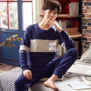 Marineblauwe katoenen tweedelige pyjama met lange mouwen gedragen door een man zittend op een bed in een huis