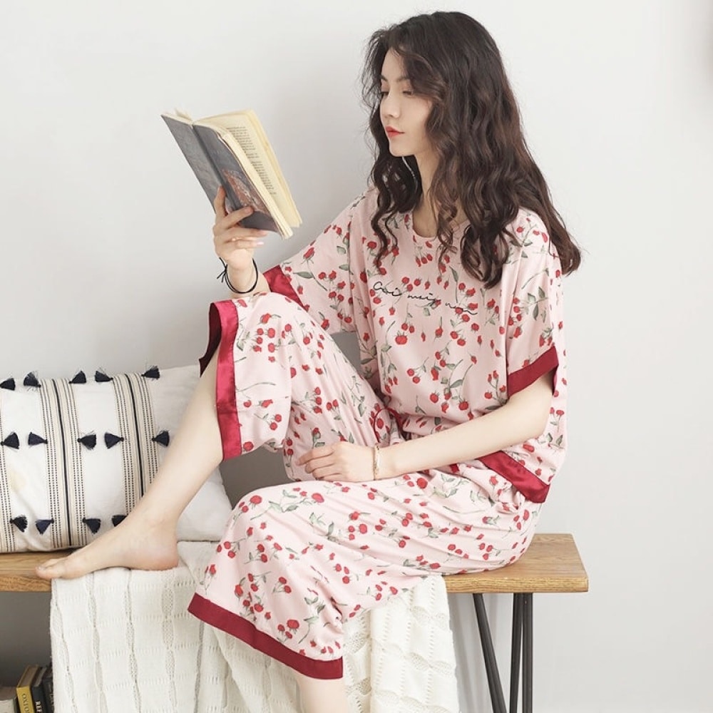 Damespyjama met vleermuismouw en rode bloemenprint gedragen door een vrouw die een boek leest zittend op een stoel in een huis