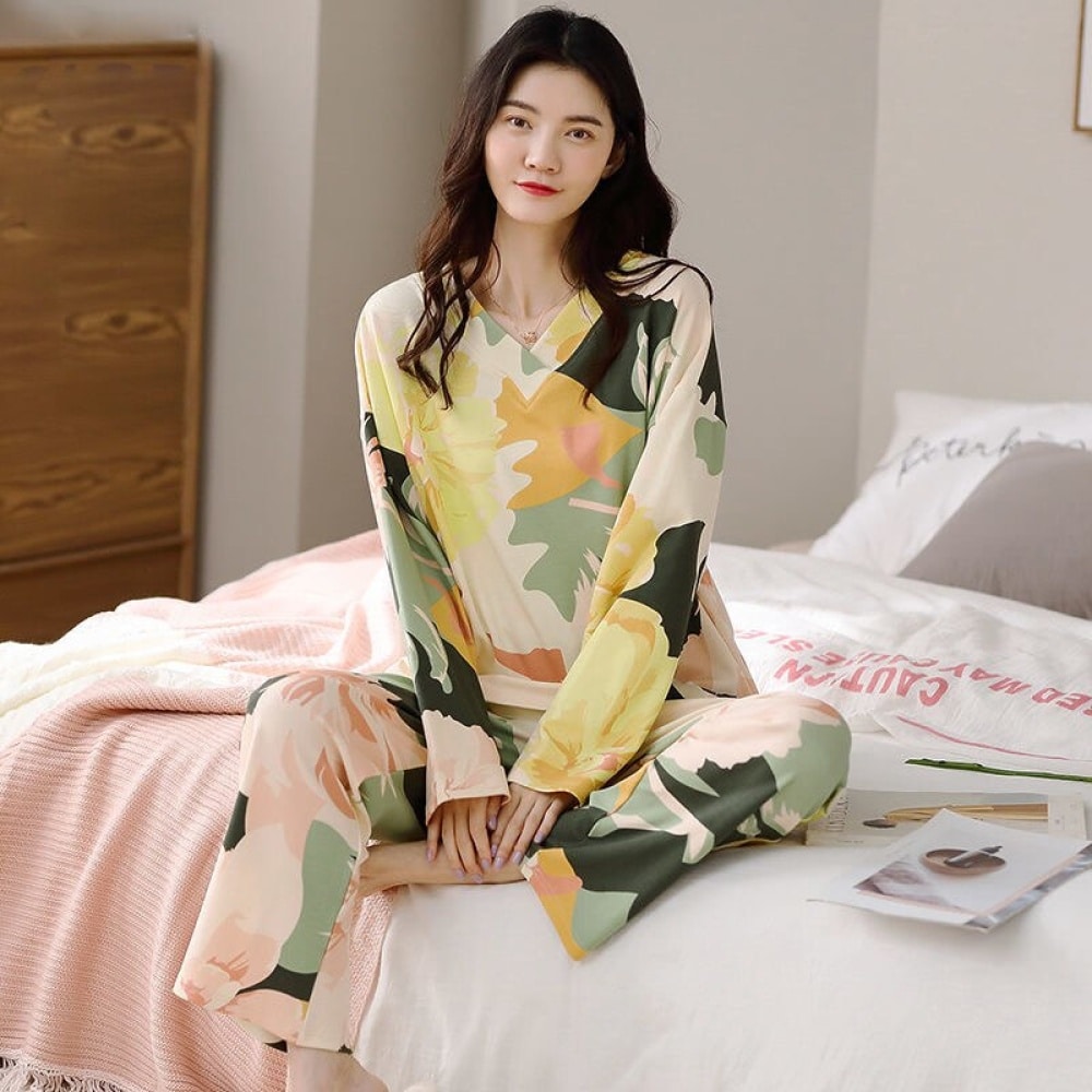 Damespyjama met lange mouwen en V-hals met bloemmotief gedragen door een vrouw zittend op een bed in een huis