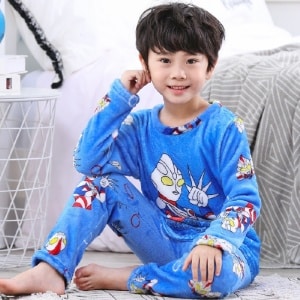 Blauwe superheldenpyjama in flanel, gedragen door een jongetje dat op een tapijt voor een bed in een huis zit