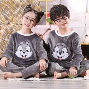 Pannenkaas flanellen pyjama voor kinderen gedragen door een kleine jongen en een klein meisje zittend op een tapijt voor een nachtkastje in een huis