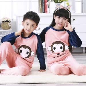 Pyjama van flanel met apenprint voor kinderen, gedragen door een jongetje en een meisje zittend op een tapijt in een huis