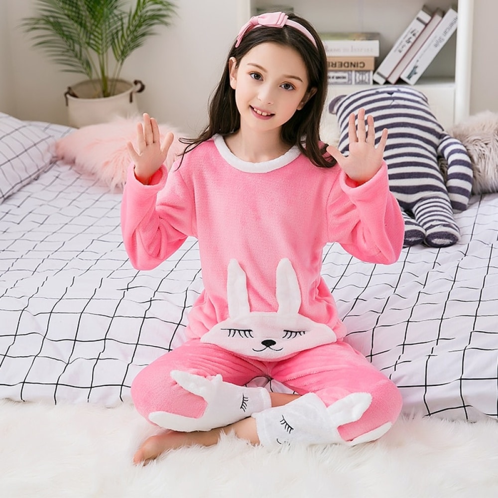 Roze flanellen pyjama met konijnenprint voor een meisje dat een hoofdband draagt zittend op een bed in een huis