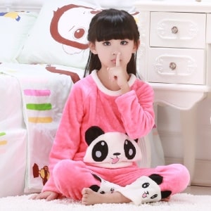 Roze tweedelige panda pyjama voor een meisje gedragen door een klein meisje zittend op een tapijt voor een bed in een huis
