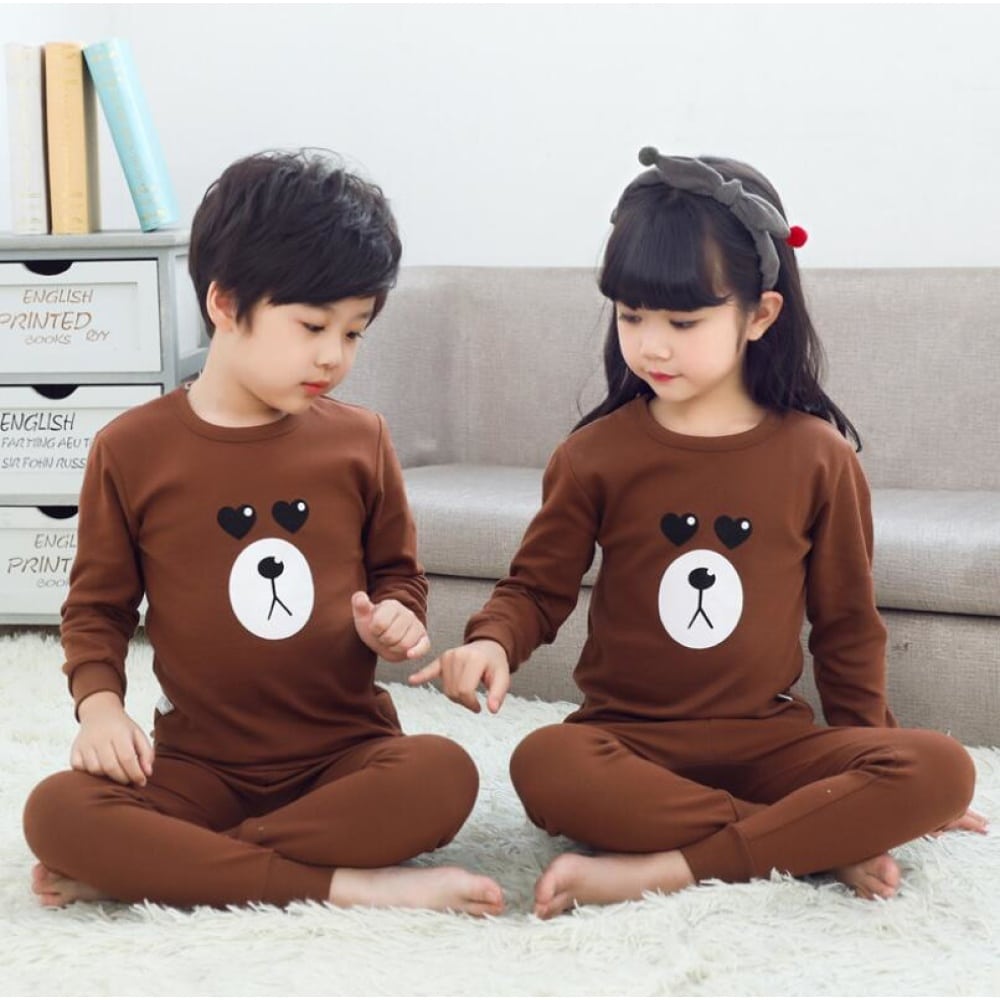 Bruine voorjaarspyjama met berenpatroon voor kinderen met twee kinderen die de pyjama dragen en een bank op de achtergrond