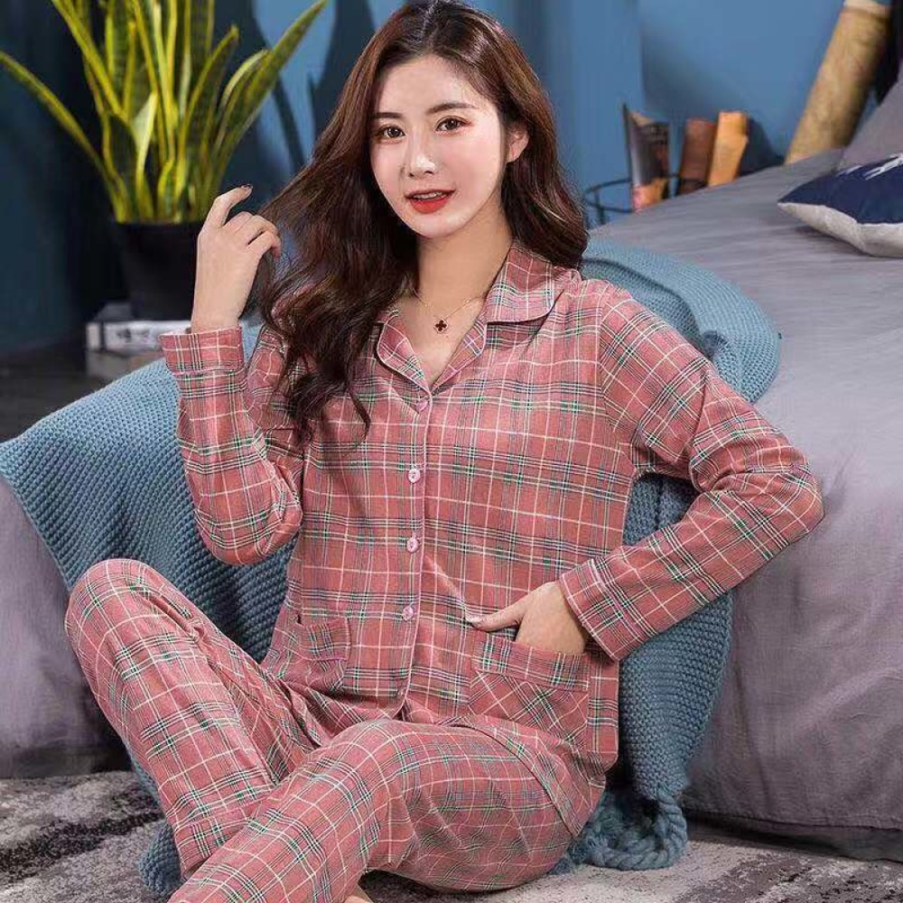 Modieuze tweedelige geruite damespyjama met omgeslagen kraag gedragen door een vrouw zittend op een tapijt voor een bed in een huis