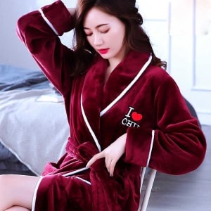Rode koraal fleece pyjama voor vrouwen van zeer hoge kwaliteit gedragen door een vrouw zittend op een stoel in een huis