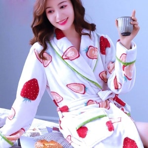 Modieuze damespyjama van aardbeienfleece, gedragen door een vrouw zittend op een bed in een huis