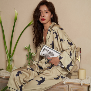 Beige panterprint pyjama gedragen door een vrouw zittend op een meubel met een tijdschrift voor een beige muur