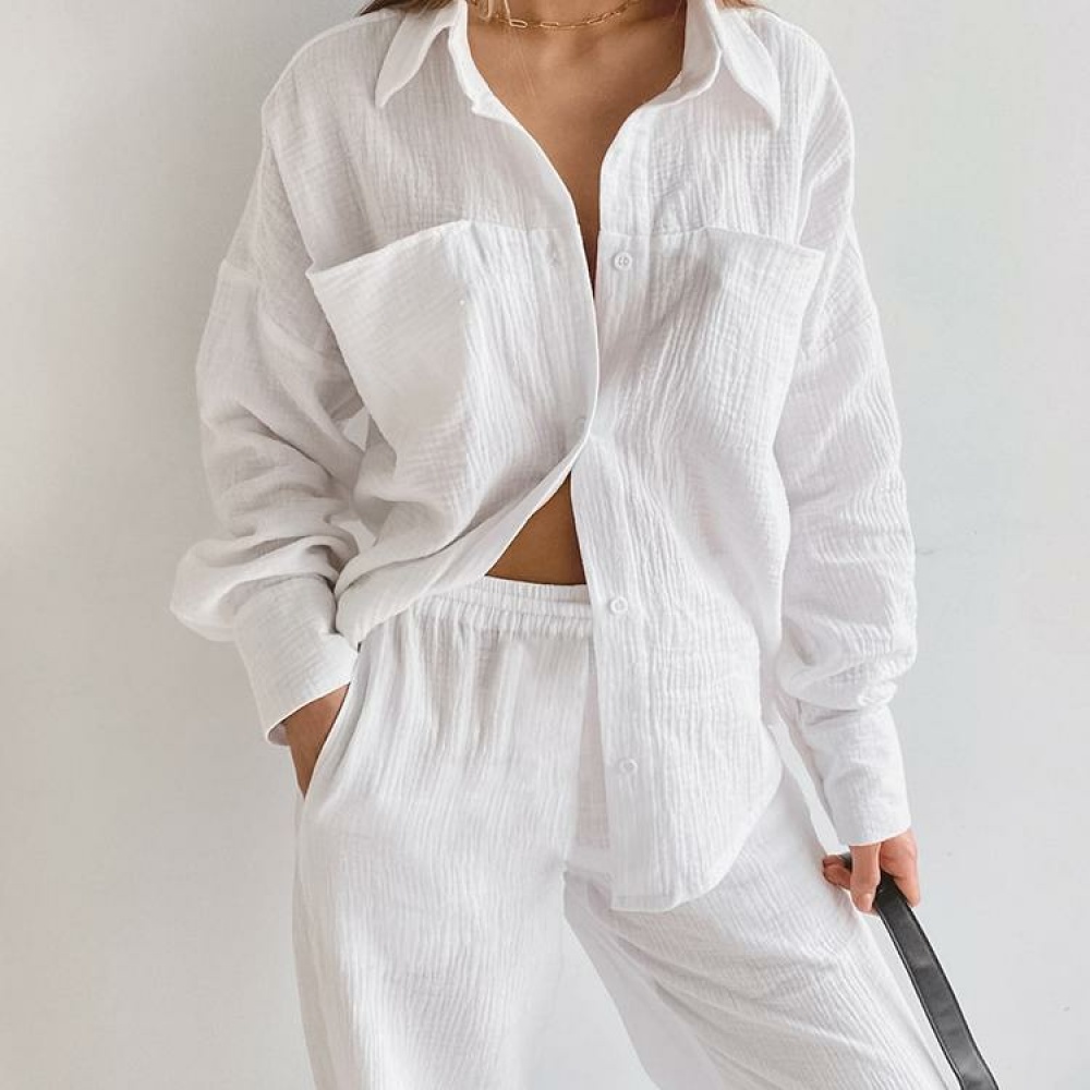Witte katoenen pyjama gedragen door een vrouw tegen een witte muur