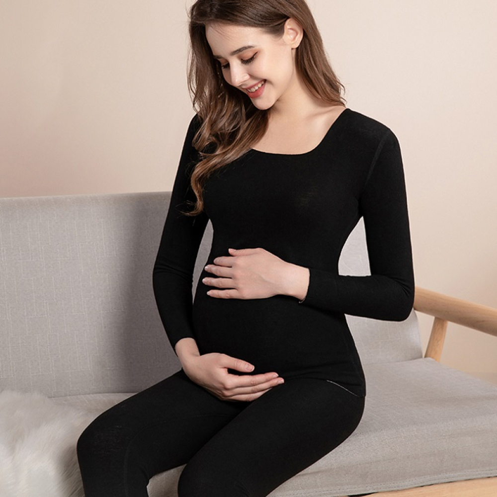 jonge zwangere vrouw in zwarte pyjama, glimlachend terwijl ze haar ronde buik aanraakt