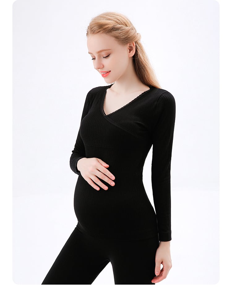 zwangere vrouw die met één hand haar buik aanraakt en een zwarte pyjama draagt bestaande uit een broek en een trui met lange mouwen
