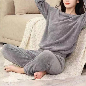 jonge vrouw in grijze pilou-pyjama, ze zit op een plaid naast een bank, op de grond, met haar handen gekruist achter haar hoofd
